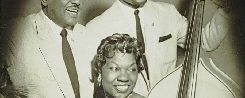 Charlotte Cowens sits at a piano with two other musicians