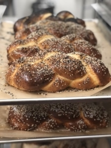 Loaves of challah stacked on baking trays, ready for pickup