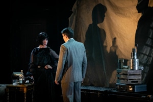 Richard Hannay speaks with a woman, their shadows looming behind them.