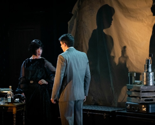 Richard Hannay speaks with a woman, their shadows looming behind them.