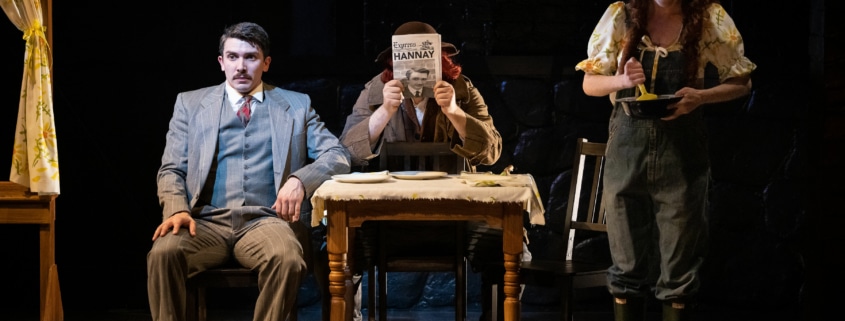 Richard Hannay seated at a table with a man reading a newspaper. The headline reads 'Hannay.' A waitress smiles, stirring something in a bowl as she looms over the table.