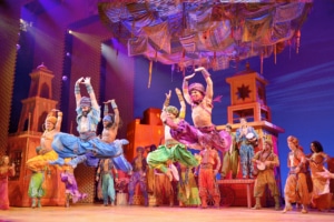 Male dancers leap through the air with their arms above their head in Aladdin.