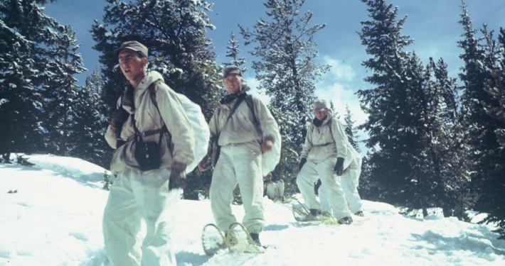 A line of soldiers snowshoe down a mountain in Camp Hale