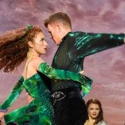 A man and woman spin, arms wrapped around each other as other dancers look on behind them in Riverdance