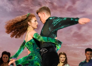 A man and woman spin, arms wrapped around each other as other dancers look on behind them in Riverdance