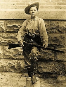 An old photograph of Pearl Hart wearing men's clothes and holding a rifle