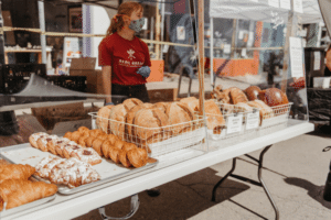 A woman stands behind a table covered in loaves of bread for sale at the farmers market