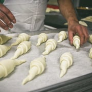 A baker places rolled croissant dough onto a baking tray