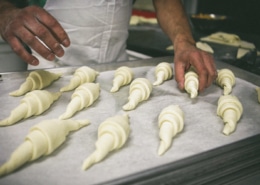 A baker places rolled croissant dough onto a baking tray