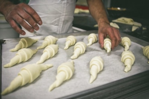 A baker places rolled croissant dough onto a baking tray