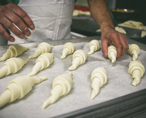 A baker places rolled croissant dough onto a baking tray