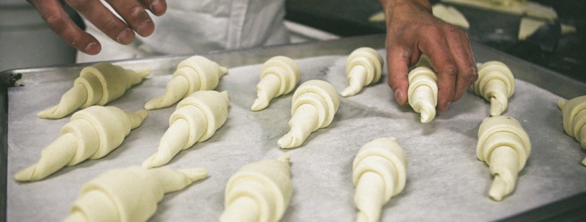 A baker places rolled croissant dough onto a baking tray