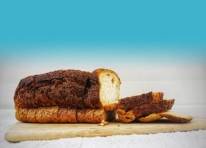 A loaf of bread with a few slices taken out sits on a cutting board in front of a blue background