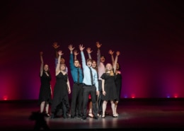 The Lead Performer nominees stand huddled together, singing the final note of the medley at the Bobby G Awards. Each has one arm raised, fingers reaching high.