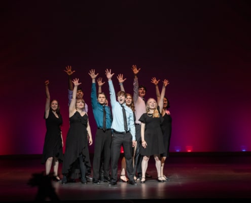 The Lead Performer nominees stand huddled together, singing the final note of the medley at the Bobby G Awards. Each has one arm raised, fingers reaching high.