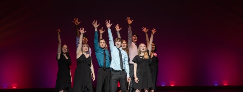 The Lead Performer nominees stand huddled together, singing the final note of the medley at the Bobby G Awards. Each has one arm raised, fingers reaching high.