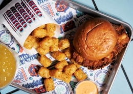 A fried chicken sandwich with a pouch of tater tots spilling on a Birdcall tray