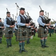 Rows of musicians playing the bagpipes wearing kilts