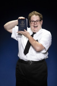 Actor Sam Nackman poses with the literal Book of Mormon, a big smile on his face