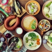 A table filled with several Scandinavian dishes, including a smoked sausage, creamy soup, roasted vegetables, fish, and more