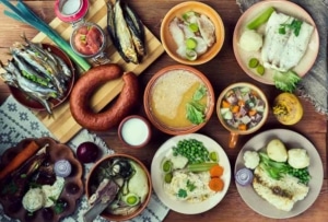 A table filled with several Scandinavian dishes, including a smoked sausage, creamy soup, roasted vegetables, fish, and more