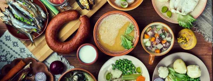 A table filled with several Scandinavian dishes, including a smoked sausage, creamy soup, roasted vegetables, fish, and more