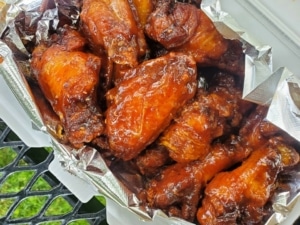 A close up of a foil packet overflowing with saucy wings