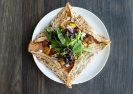 A crepe folded in a square around colorful filling, a green garnish on top