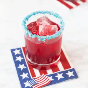 Blue pop rocks rim a red cocktail, sitting on a US flag themed napkin