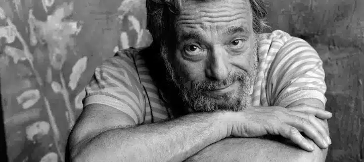 Stephen Sondheim leaning over the back of a chair, smirking at the camera