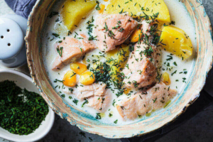 A large pot of creamy soup, made with salmon and potatoes. A sprinkling of green herbs brightens the bowl.