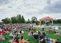 Hundreds of people sit on the grass, on blankets and in chairs. There is a band playing in a small gazebo.