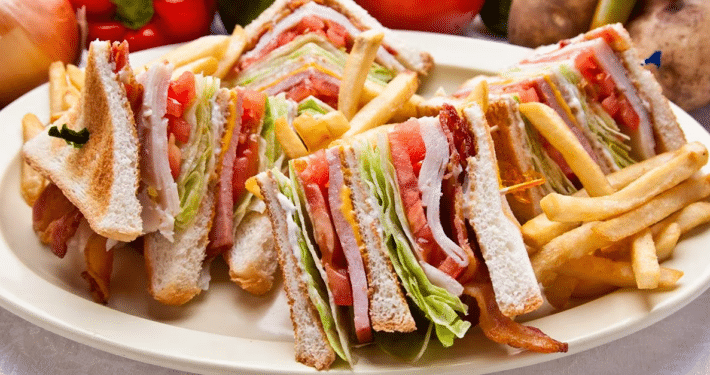 A triangularly sliced club sandwich on a large plate with french fries