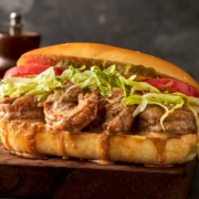 A dressed shrimp po' boy sits on a cutting board. It is dripping gravy