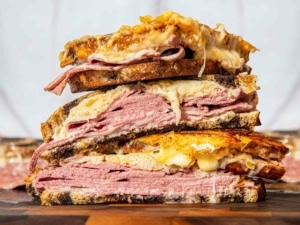 A sliced Reuben sandwich stacked up high. The cheese is melting out of the bread