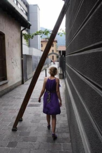 A woman in a purple dress walks under a ladder leaning against a building