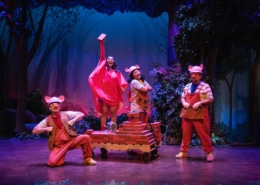 The Three Little Pigs and Little Red pose with the cart full of bricks. Little Red is holding one brick high in the air.