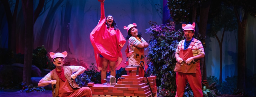 The Three Little Pigs and Little Red pose with the cart full of bricks. Little Red is holding one brick high in the air.