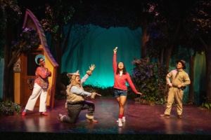 Little Red's mom, the Wolf, Little Red, and the Park Ranger sing onstage together. Everyone is looking at Little Red, who stands in the center, smiling.