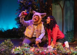 The Wolf holds up a fresh tomato plucked from the garden in front of him. Little Red kneels next to him, smiling at the produce.