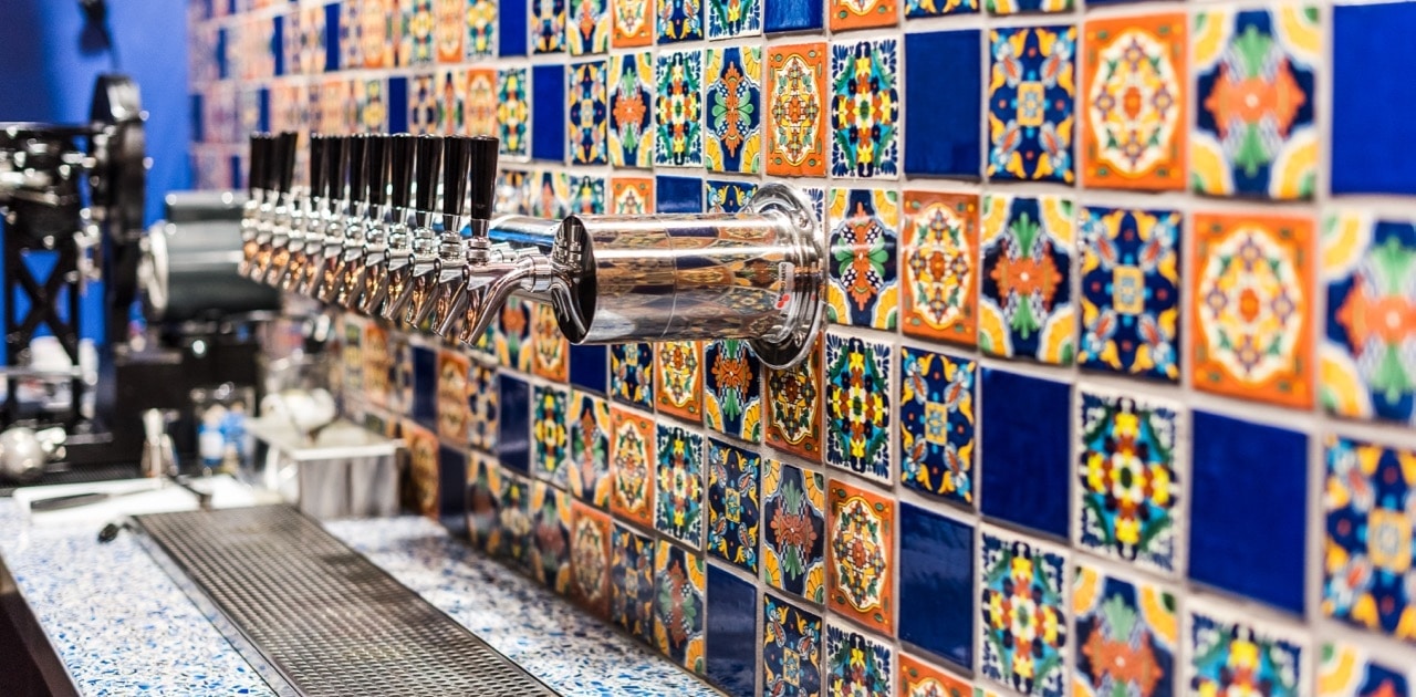 The taps at Cheluna in Stanley Marketplace. They are set into a orange and blue tiled wall.