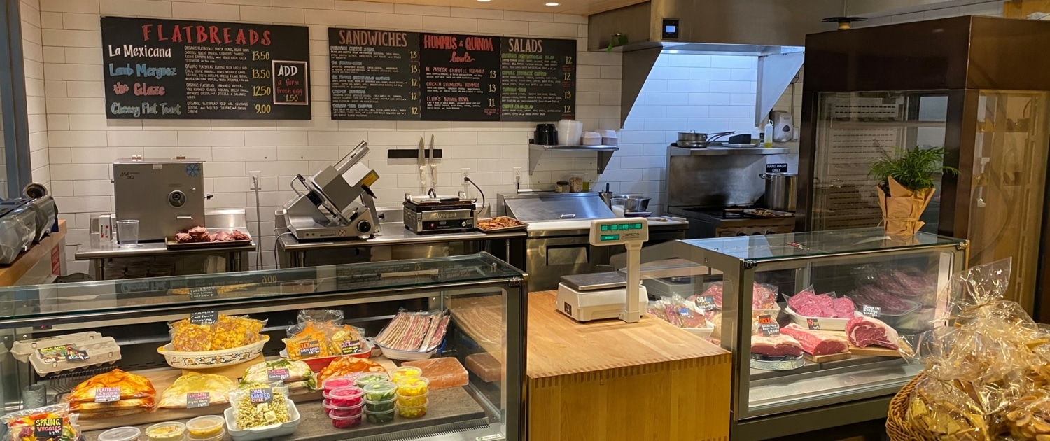 The counter inside Elita Specialty Market. On the left is a display of salads and dips. On the right is a selection of meats.