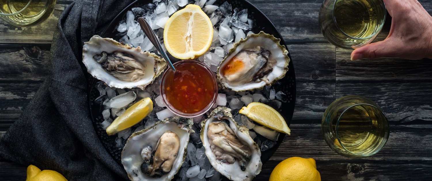 Platter of oysters, lemon slices, and sauce atop ice