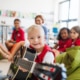 A down-syndrome boy with school kids and teacher sitting on the floor in class, playing guitar.