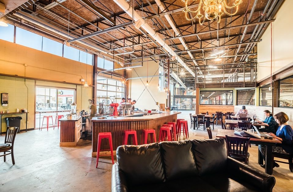 The interior of Logan House Coffee at Stanley Marketplace. Red stools line the central bar area, and people are seated in booths along the edge.