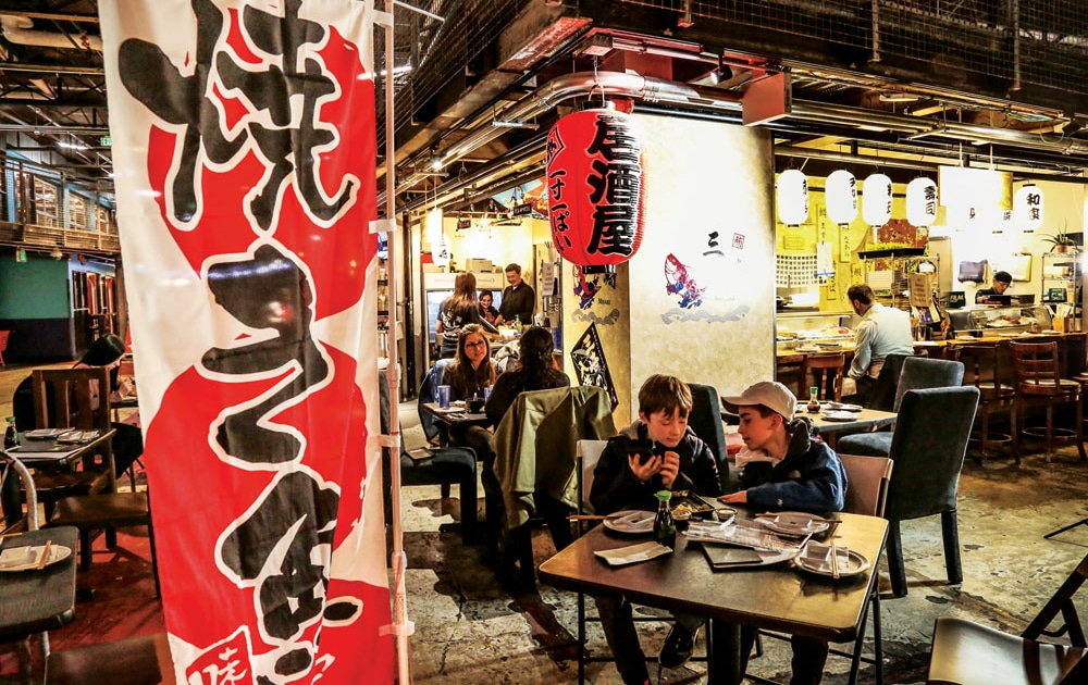 People eat at tables outside Misaki in Stanley Marketplace. In the foreground, there is a large red banner with black Japanese writing