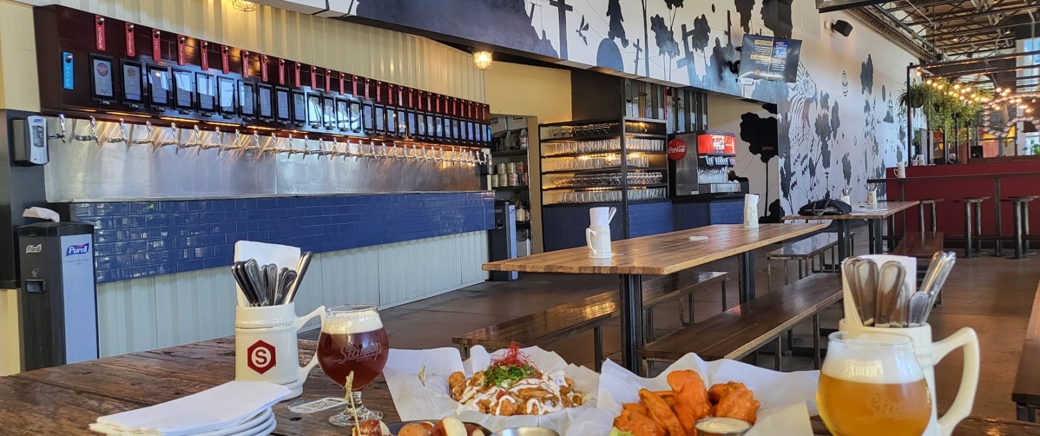 A table is filled with beer and food at Stanley Beer Hall. In the background, you can see a row of pour-you-own taps.