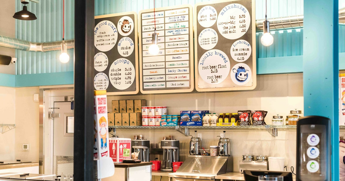 Sweet Cow at Stanley Marketplace. There is a row of menus against a light blue wall. Colorful ice cream toppings are lined up below the menus.