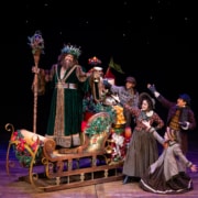 A group of townspeople surround the Ghost of Christmas Present on his sleigh