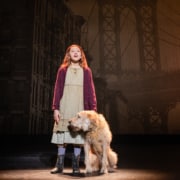 A young girl in raggedy clothes stands with a sandy-colored shaggy dog.